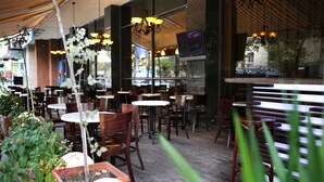 An outdoor dining area with wooden tables and chairs, potted plants, and hanging lights. - Ani Plaza Hotel (Yerevan)