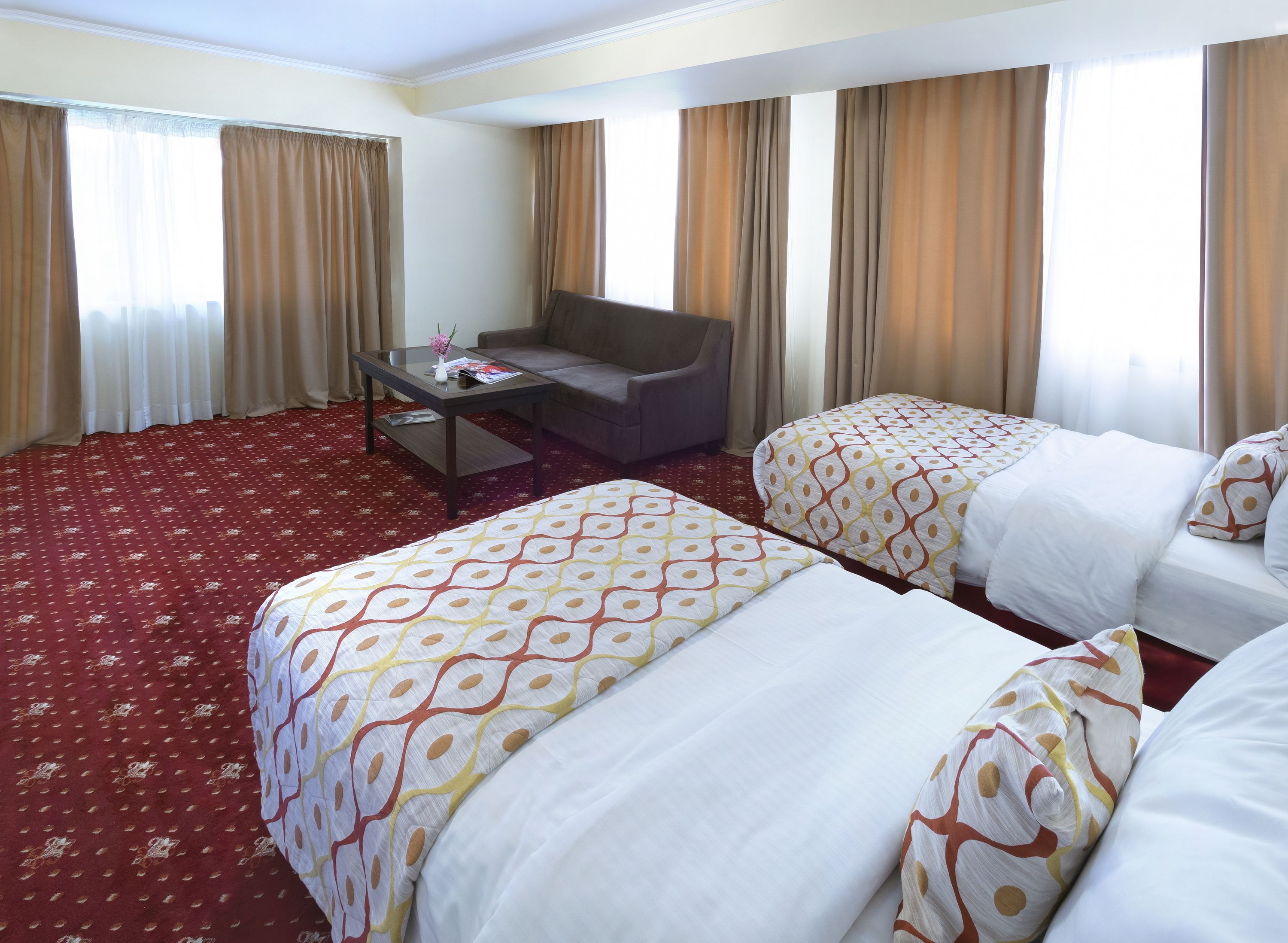 A hotel room with two beds, a sofa, a small table, and a window with curtains.
