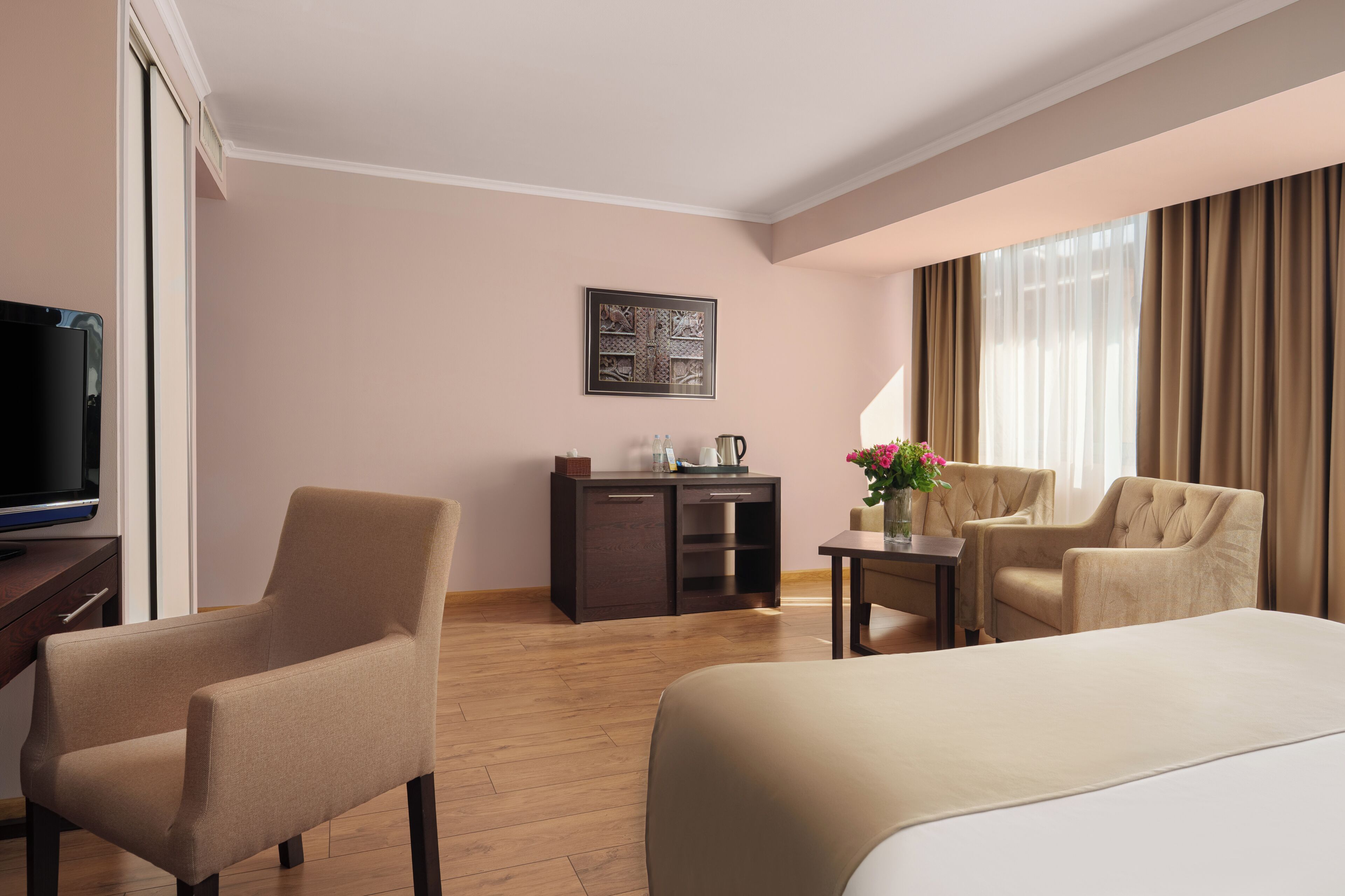 Habitación de hotel con cama, dos sillones, un escritorio con computadora, televisión y un cuadro en la pared.