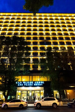 Un hôtel à plusieurs étages, avec des fenêtres illuminées et une enseigne indiquant « ANI PLAZA HOTEL ».