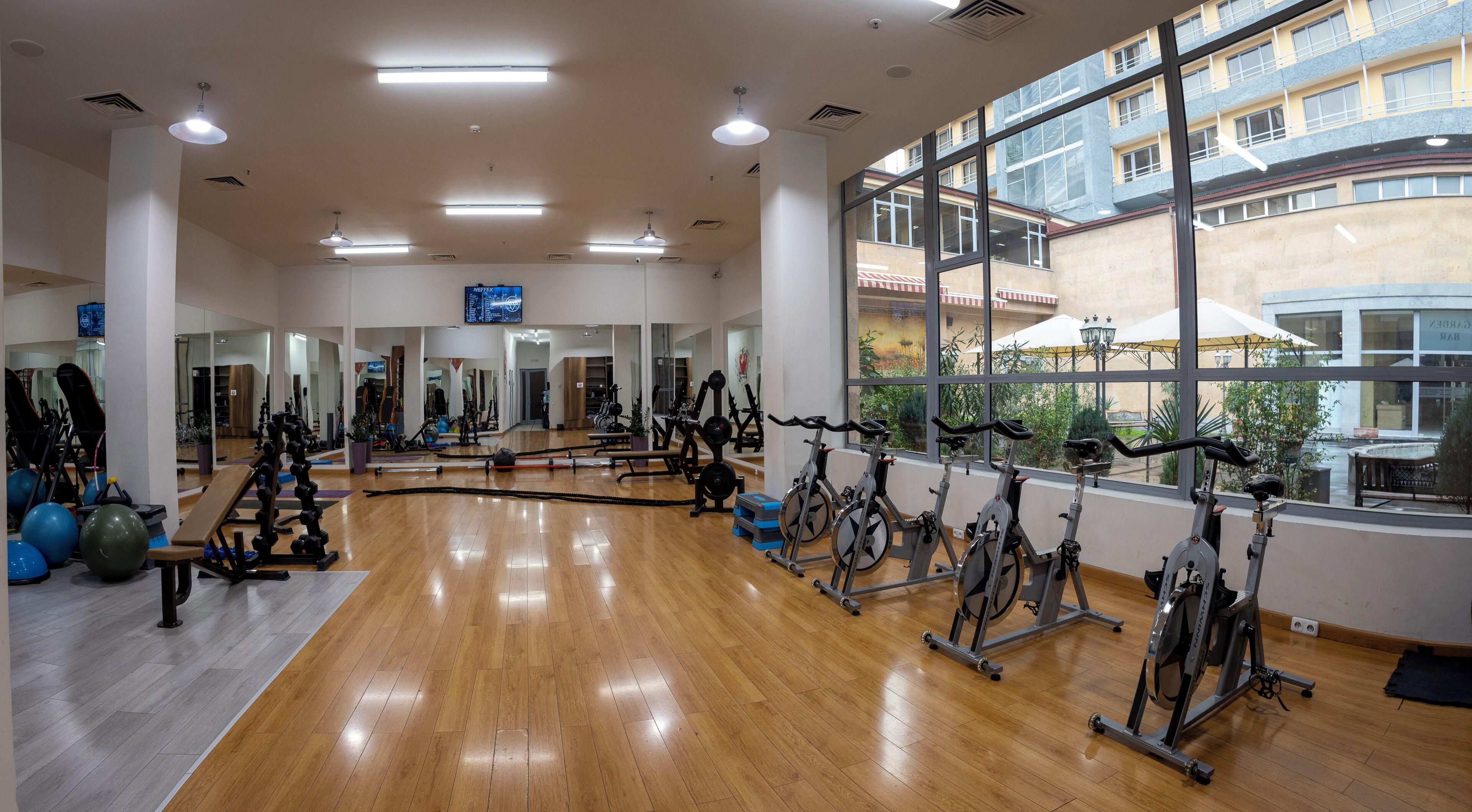 A gym with exercise equipment, wooden flooring, and large windows.