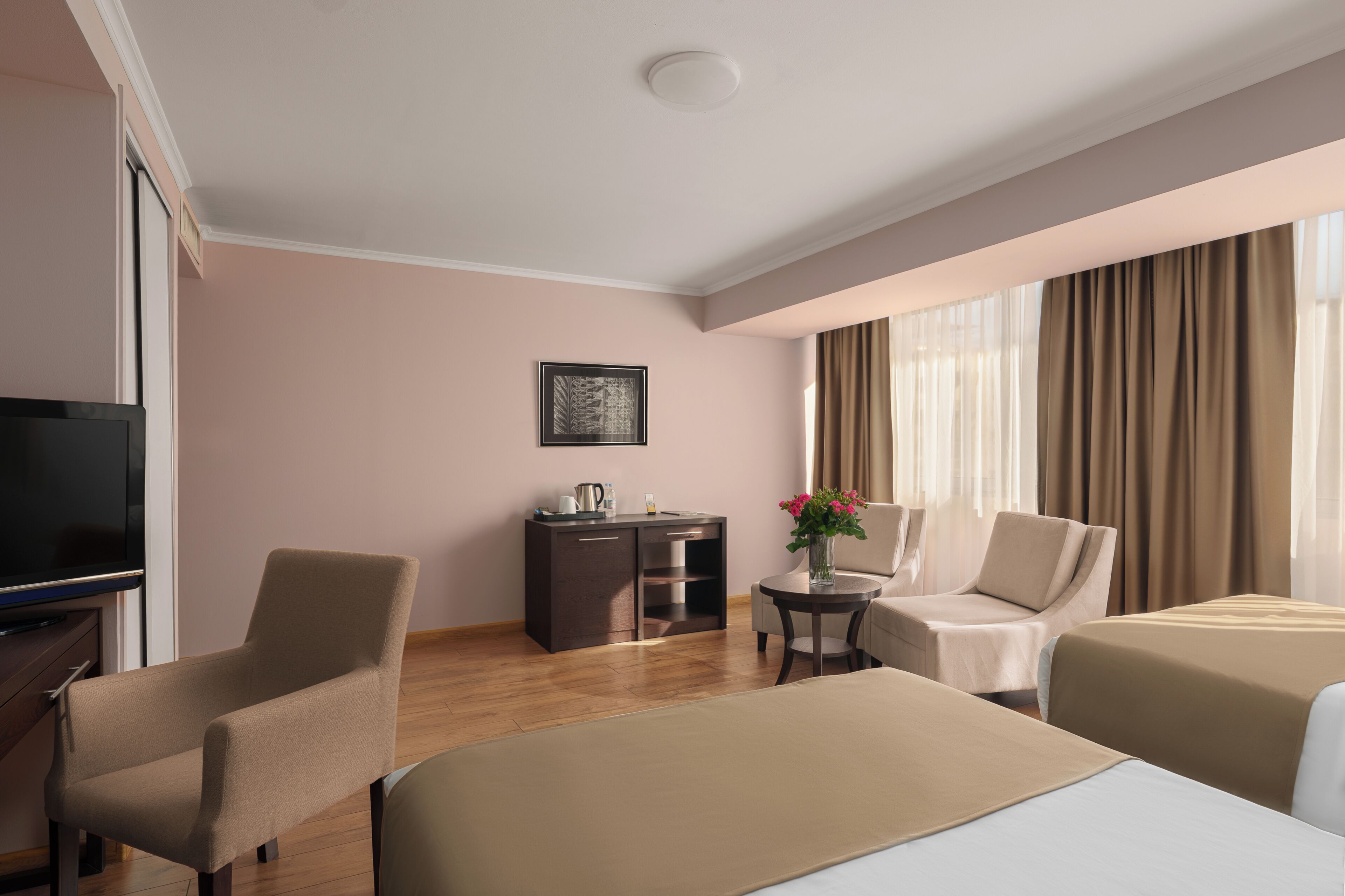 A hotel room with a bed, a desk, a chair, a TV, and a window with curtains.