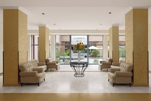 A lobby with a 'Garden Bar' sign, two sofas, a round table, and a view of the garden through large windows. - Ani Plaza Hotel (Yerevan)