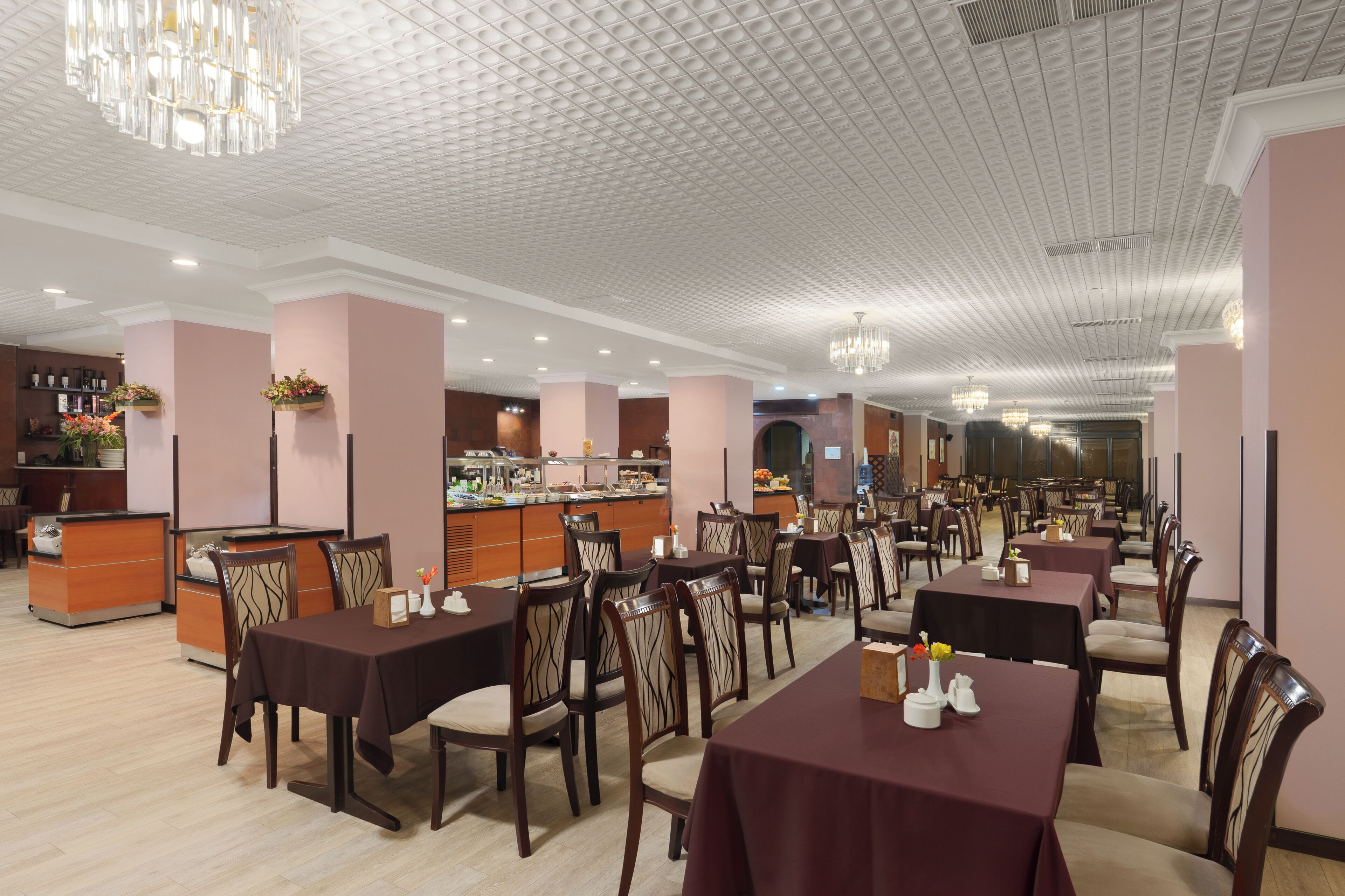A restaurant with multiple tables and chairs, a bar area, and a ceiling with a unique pattern.