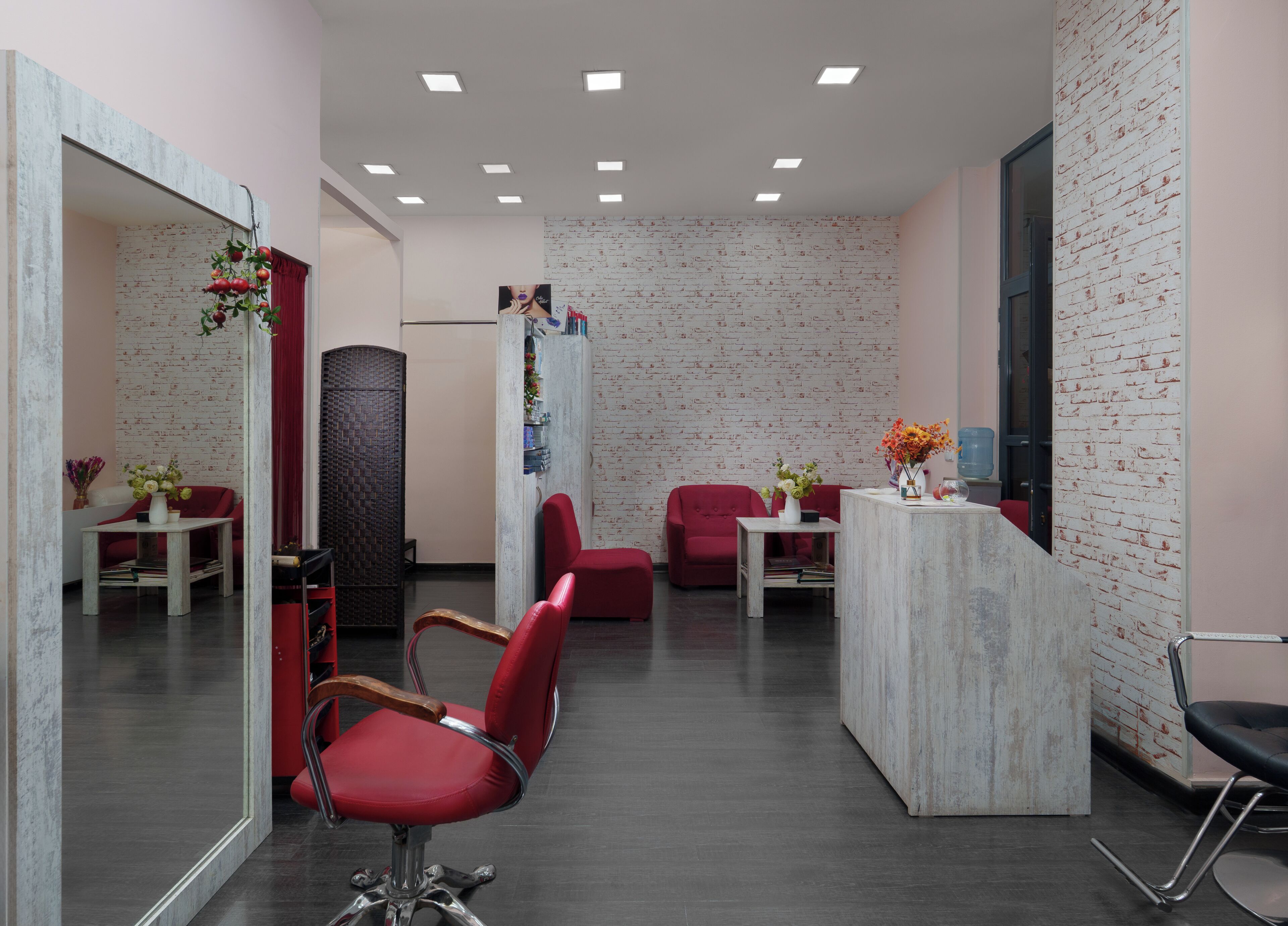 Un intérieur moderne avec un comptoir d’accueil, des chaises rouges, un miroir et un mur décoré d’un motif en briques.