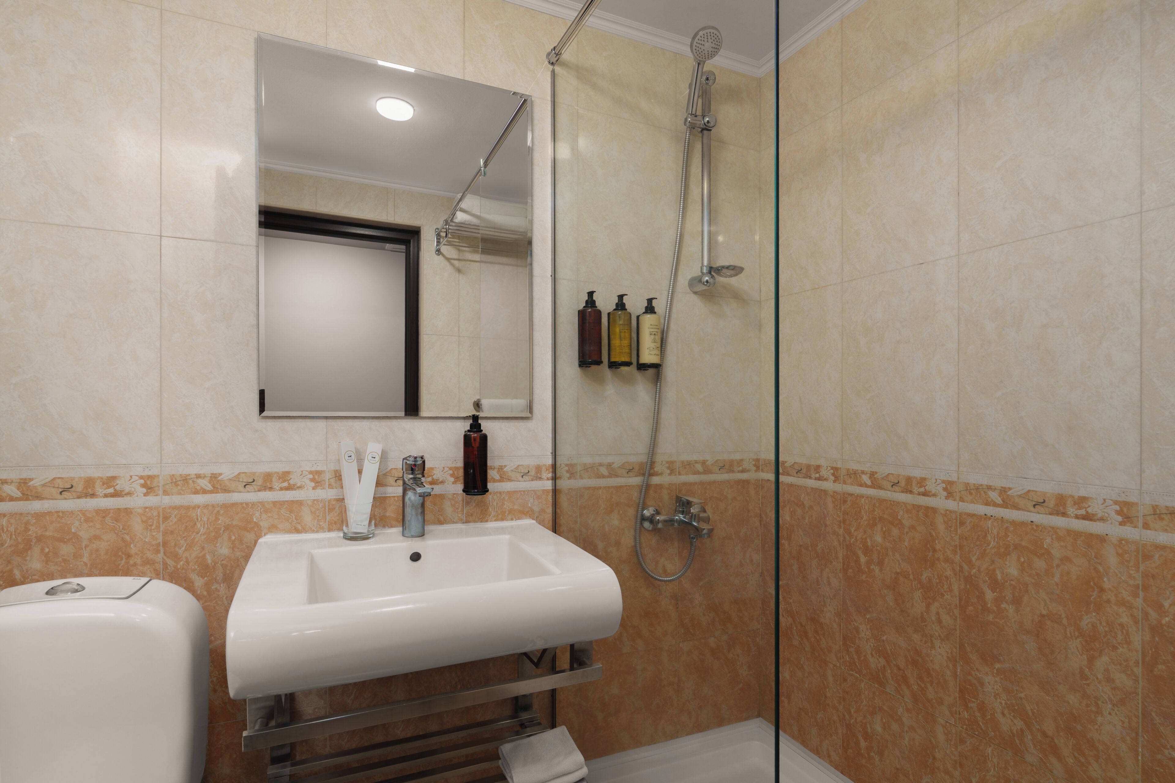 Un baño con lavamanos, espejo, ducha y artículos de aseo.