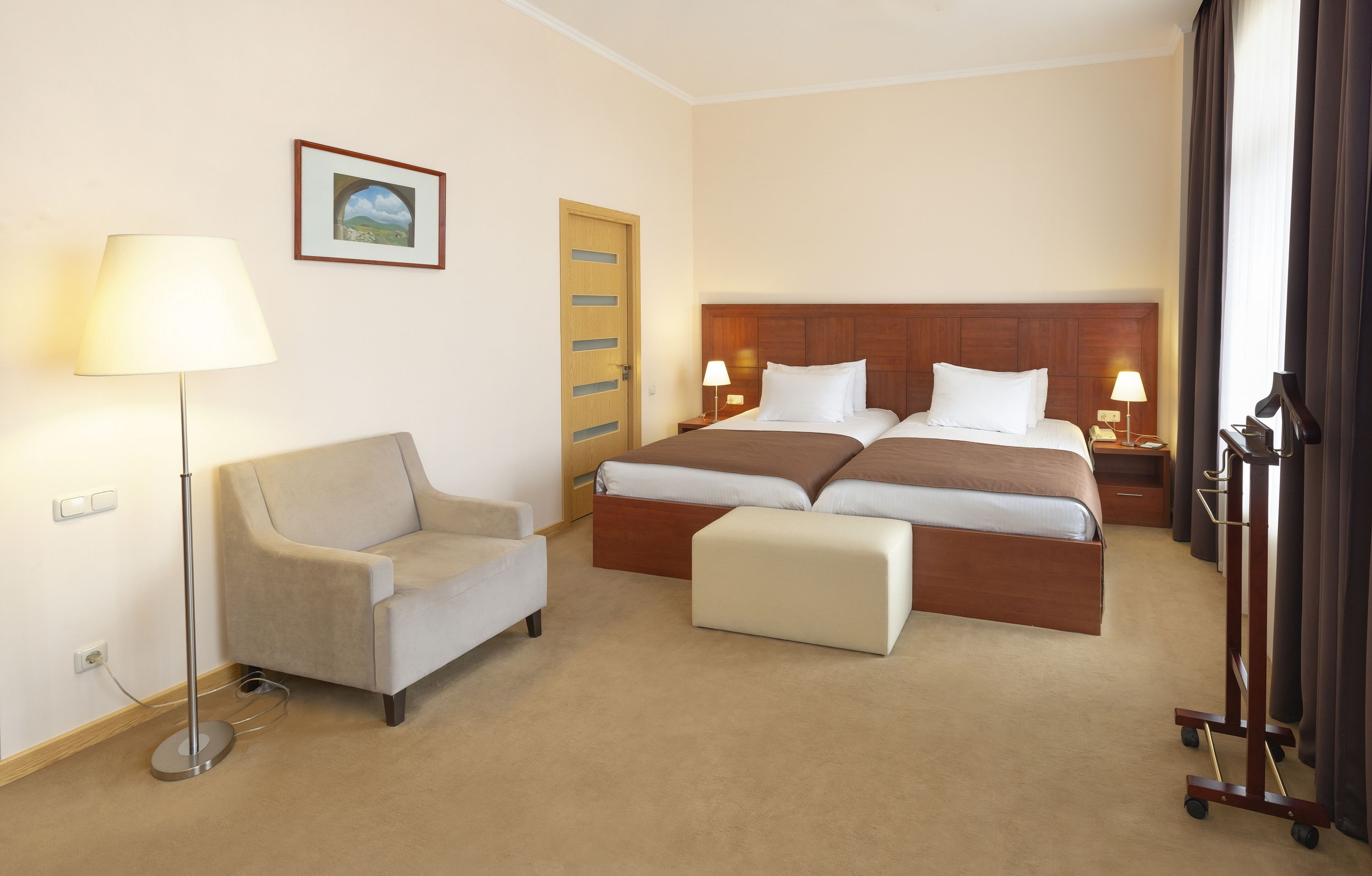 A hotel room with two beds, a sofa, a lamp, a picture on the wall, and a door.