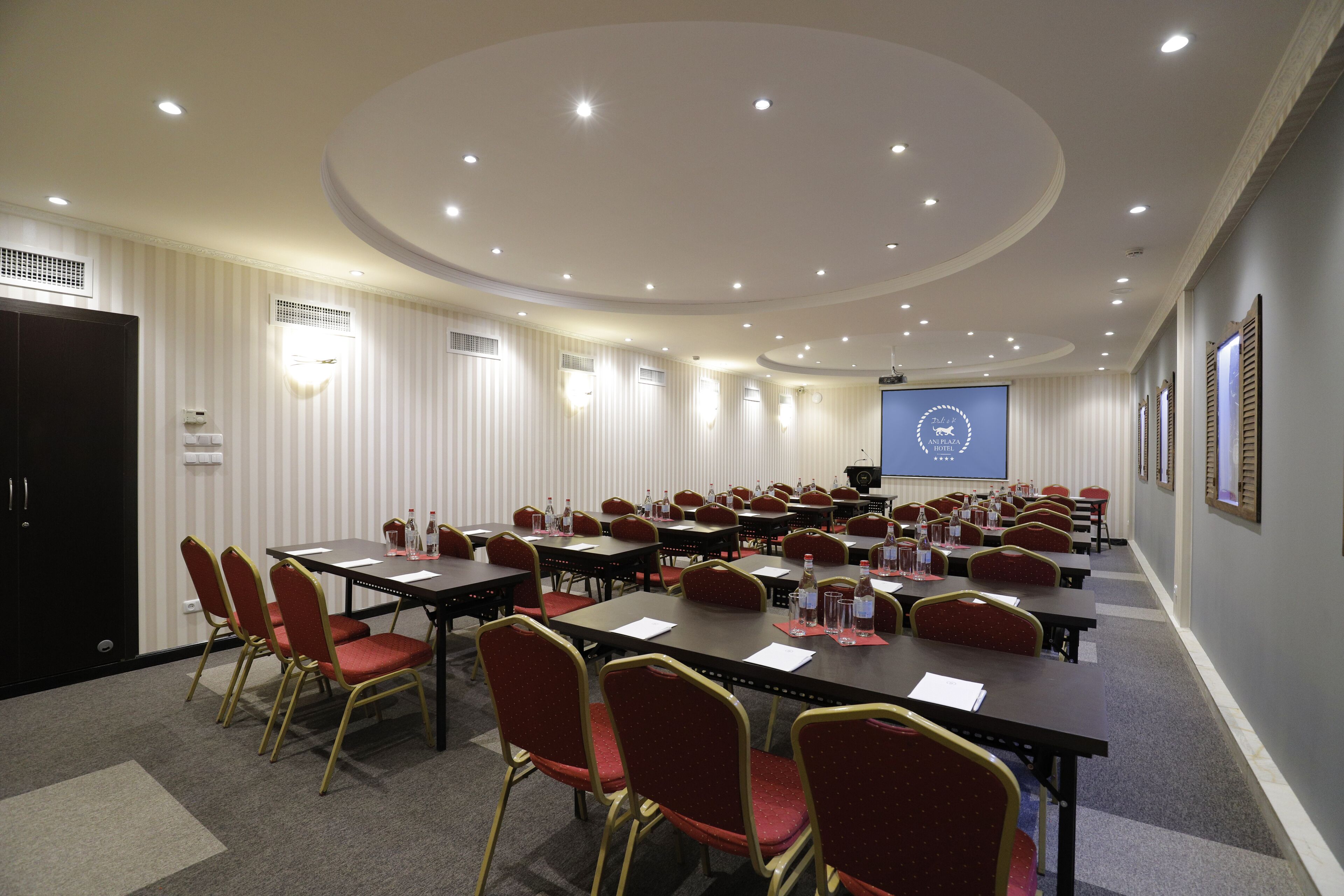 A conference room with multiple tables and chairs, a projector screen, and a podium.
