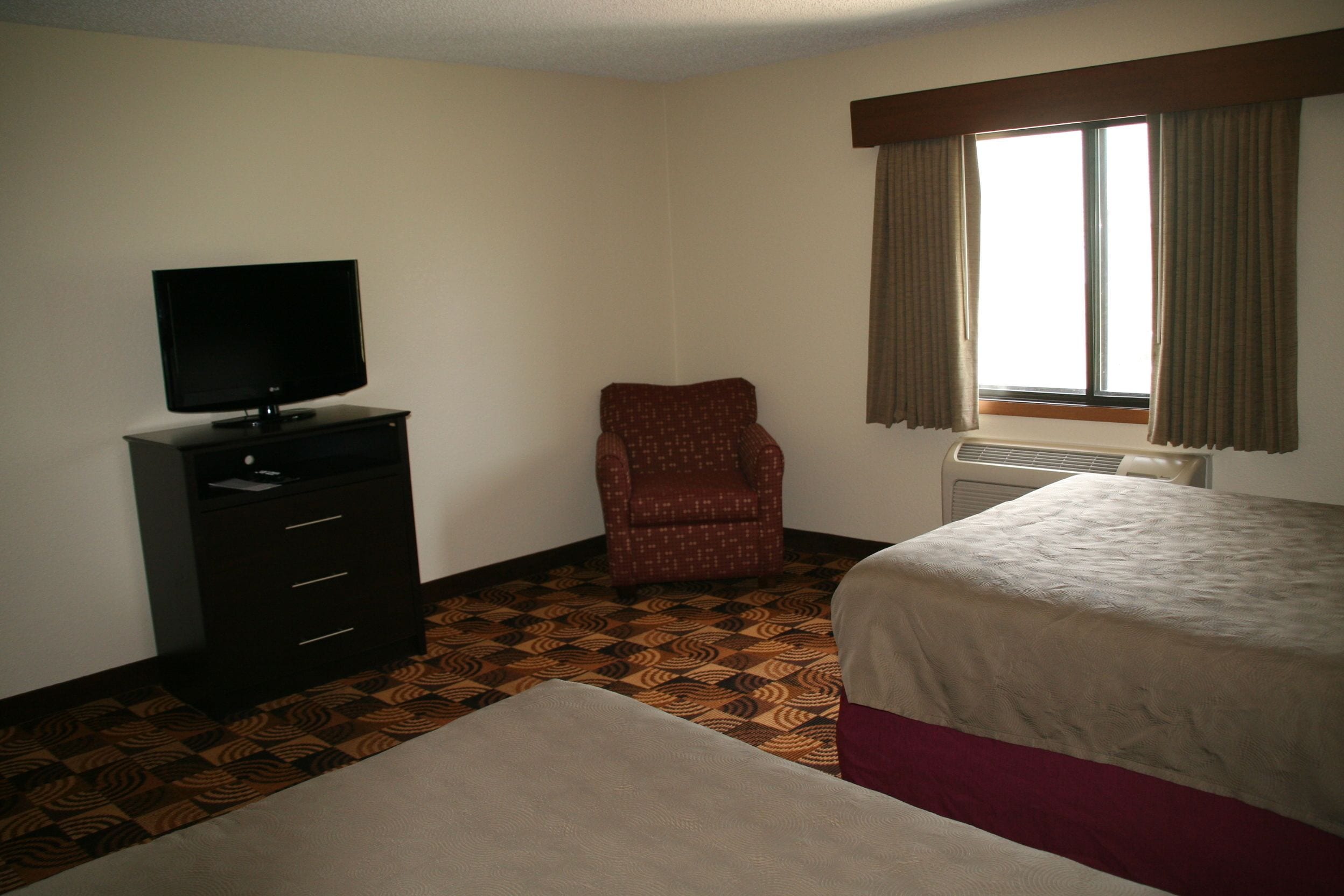 Una camera d'albergo con un letto, una televisione su un comò, una sedia e una finestra con tende.