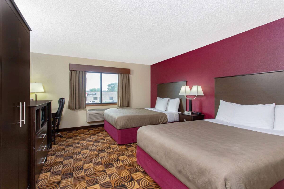 A hotel room with two beds, a desk, a chair, a window with curtains, and a patterned carpet.