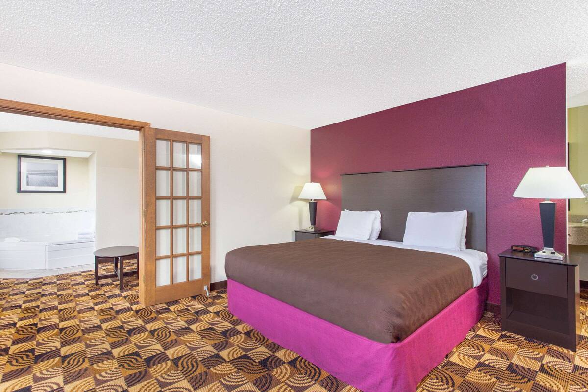 A hotel room with a bed, two bedside tables with lamps, a door, and a patterned carpet.