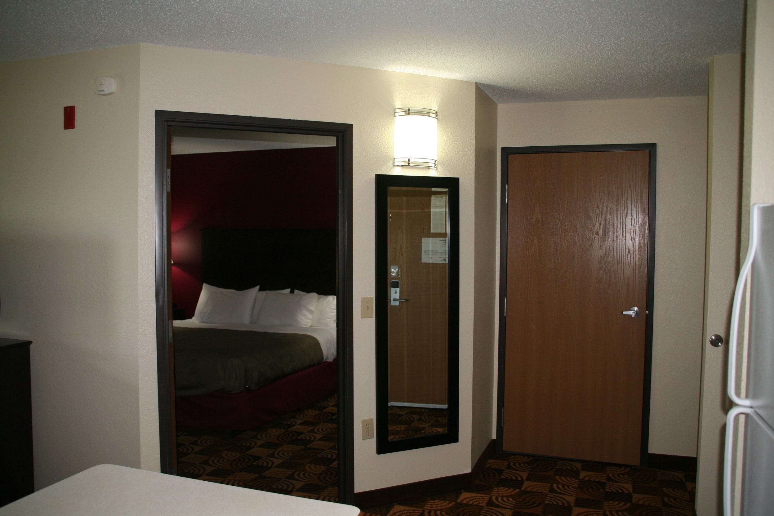 A hotel room with a bed, a mirror, a door, and a light fixture.