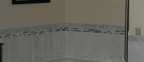 A bathroom with a white bathtub, a framed picture on the wall, and a tiled shower area.