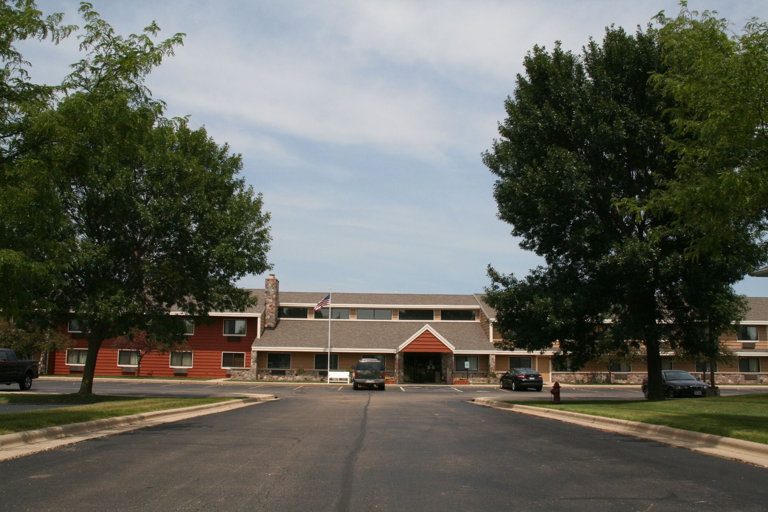 A two-story building with a red brick facade, a central entrance with a red awning, and a flagpole with an American flag.