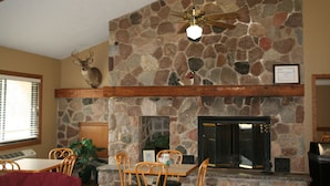 Una chimenea de piedra con ventilador de techo, sillas de madera y una mesa en un comedor.