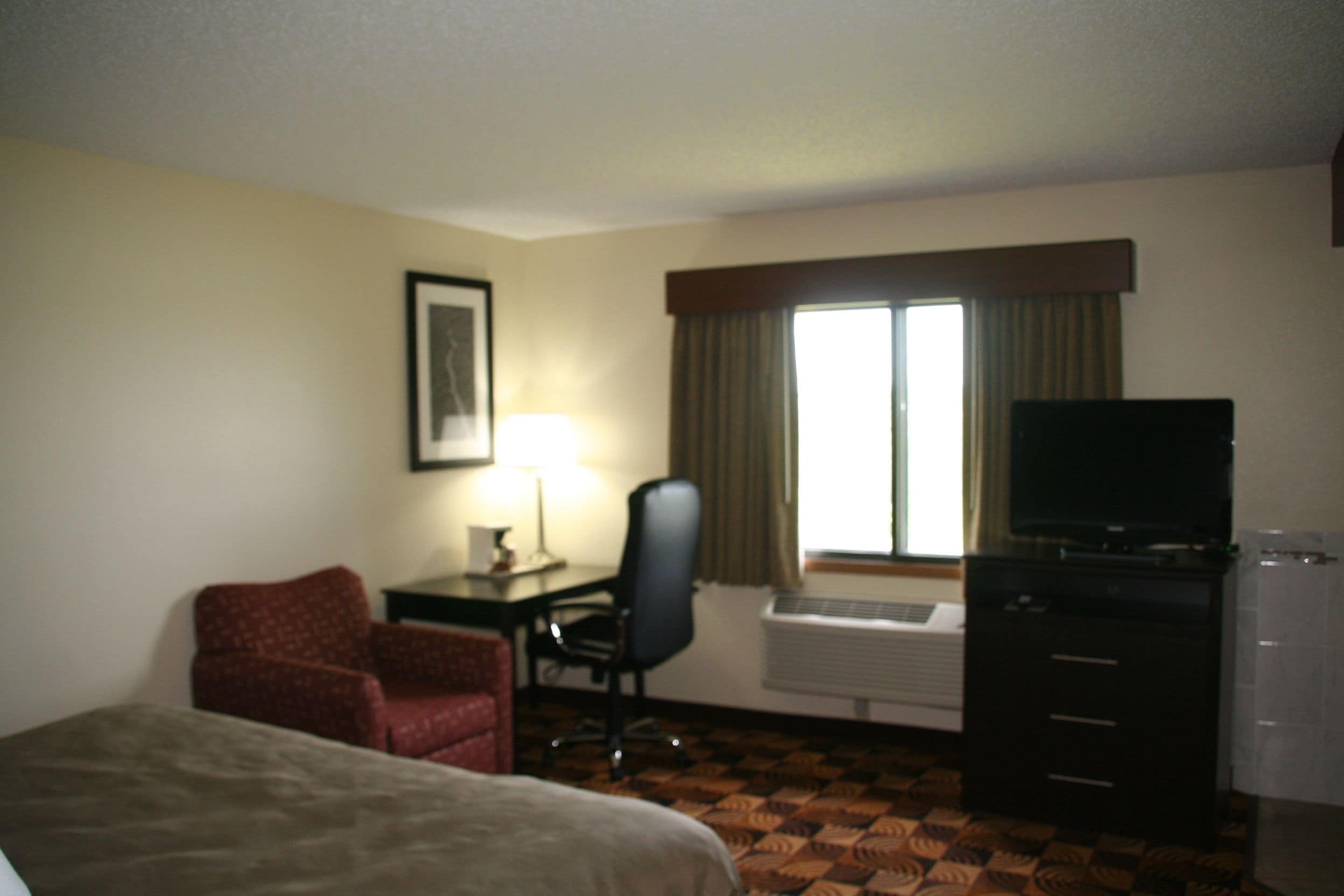 Une chambre d’hôtel équipée d’un lit, d’un bureau avec une chaise, d’une télévision et d’un appareil de climatisation.
