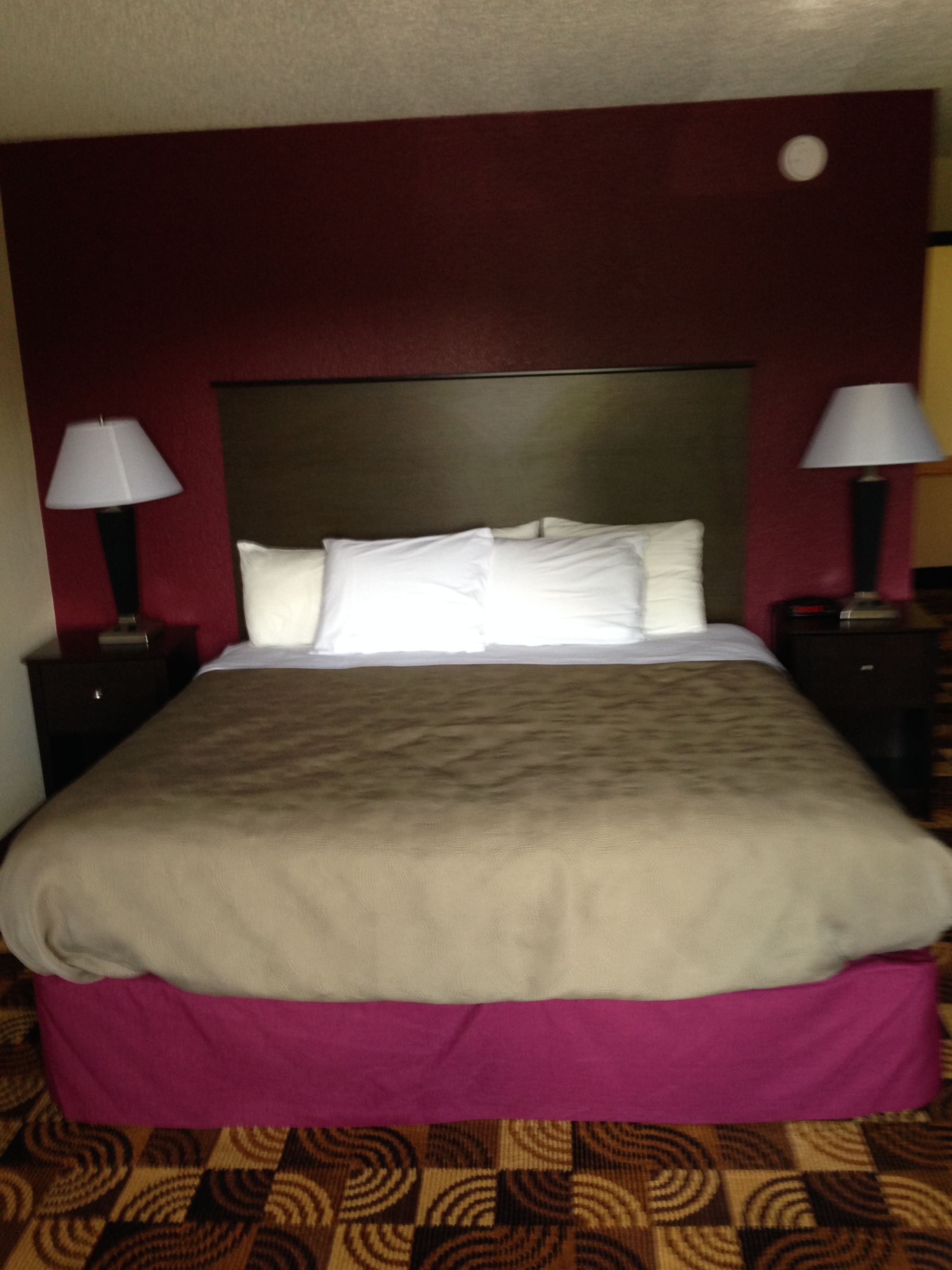 Una habitación de hotel con una cama grande, dos mesitas de noche con lámparas y un cabecero.
