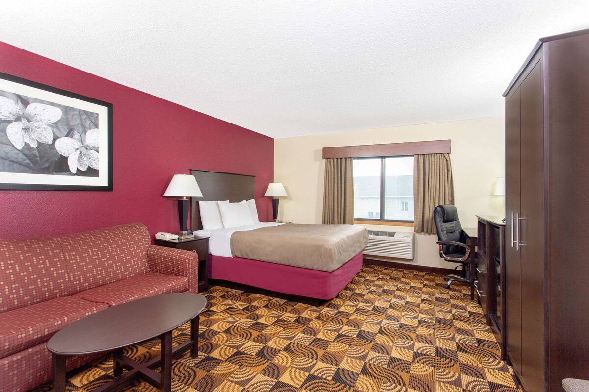 A hotel room with a bed, a sofa, a desk, a chair, and a large window with curtains.