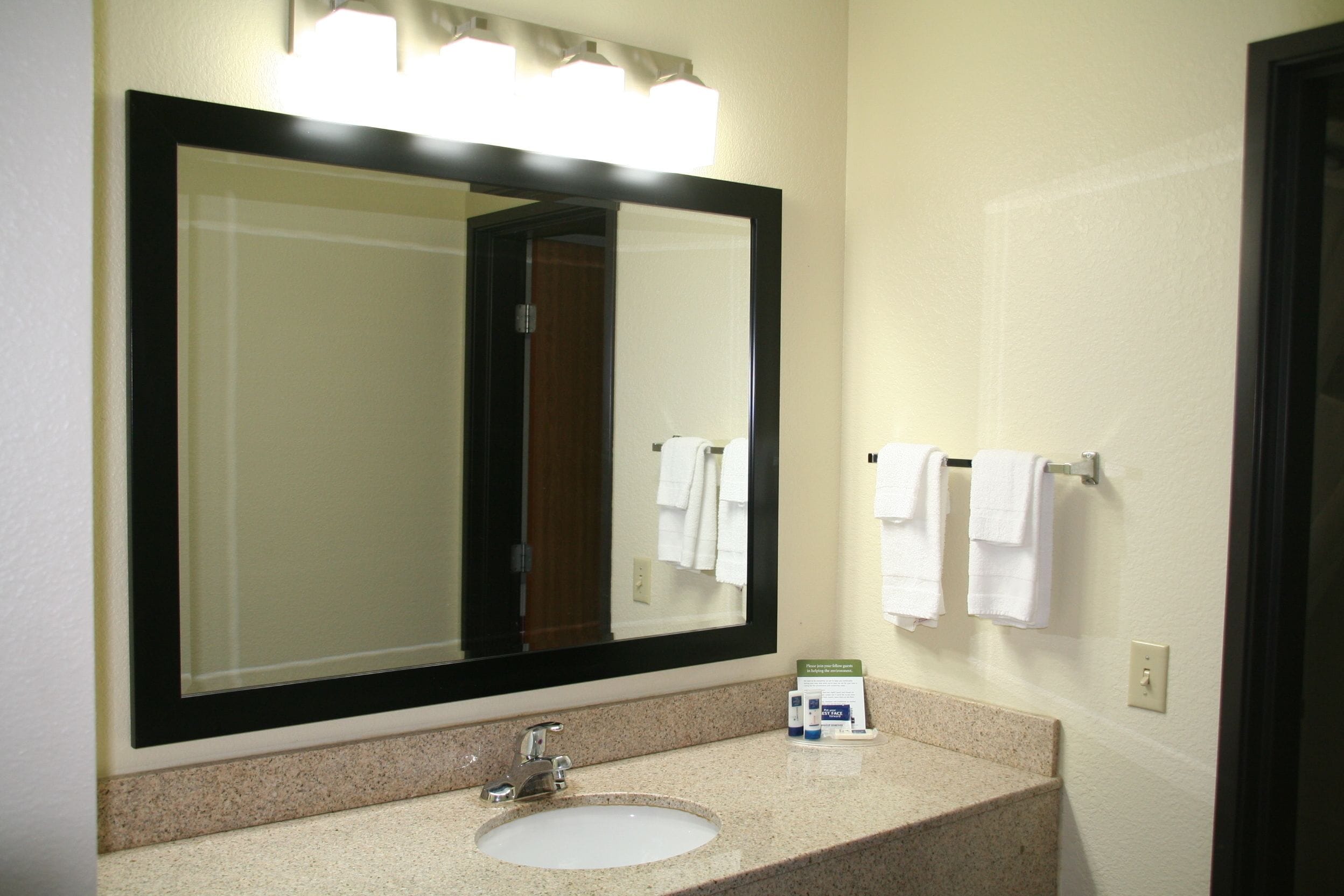 Un baño con un espejo grande, un lavabo y dos toallas colgadas en un perchero.
