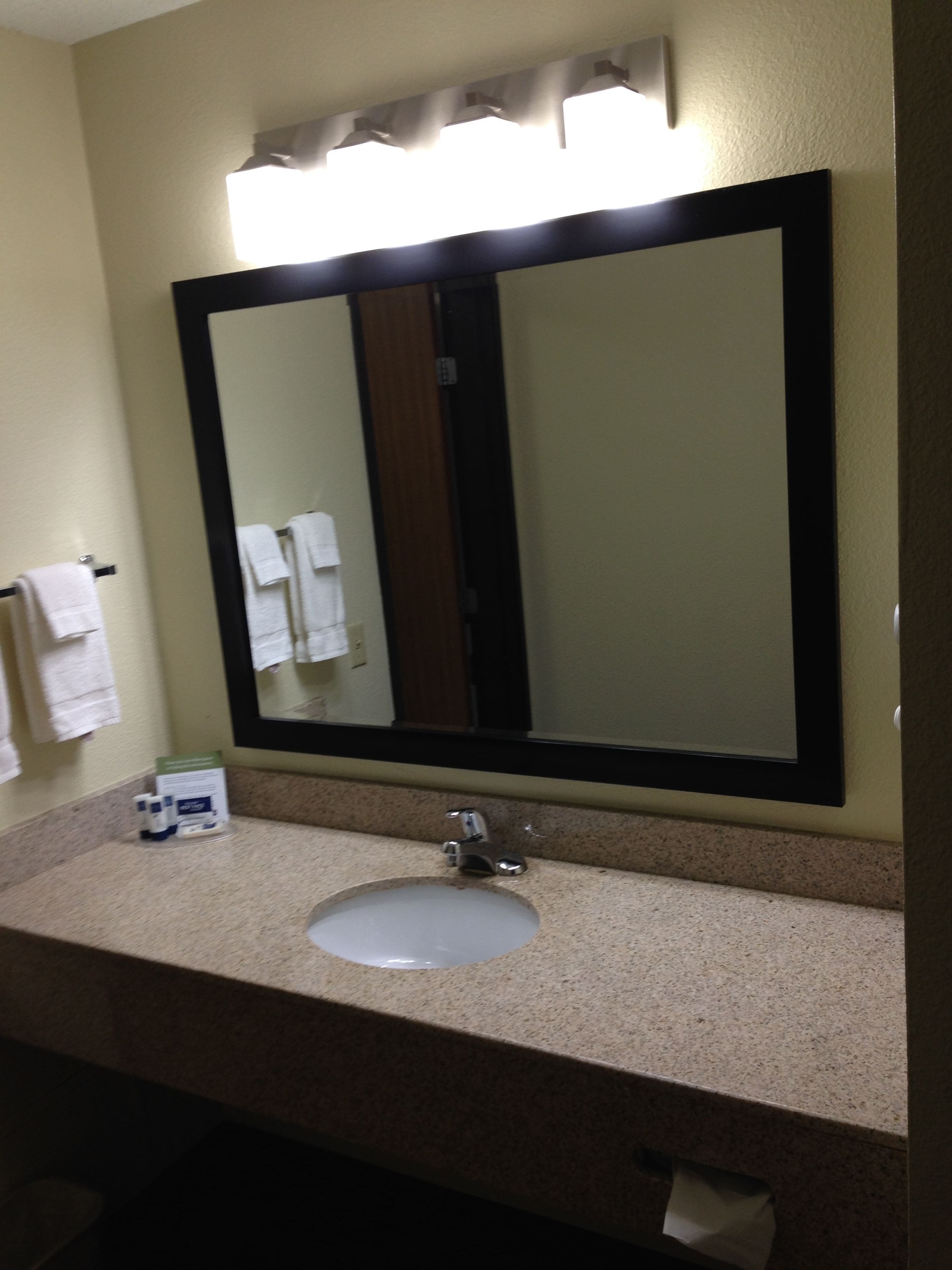 A bathroom with a large mirror, a sink, and a towel rack with towels.