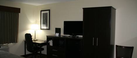 Habitación de hotel con cama, escritorio, silla, televisor, armario y un cuadro en la pared.