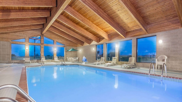 Una piscina interior con vigas de madera, ventanas amplias y sillones de descanso.