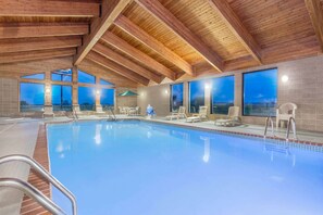 An indoor swimming pool with wooden beams, large windows, and lounge chairs. - AmericInn by Wyndham Elkhorn Near Lake Geneva (Elkhorn)