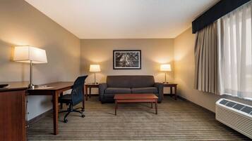 Habitación de hotel con escritorio, silla de oficina, sofá y dos lámparas.