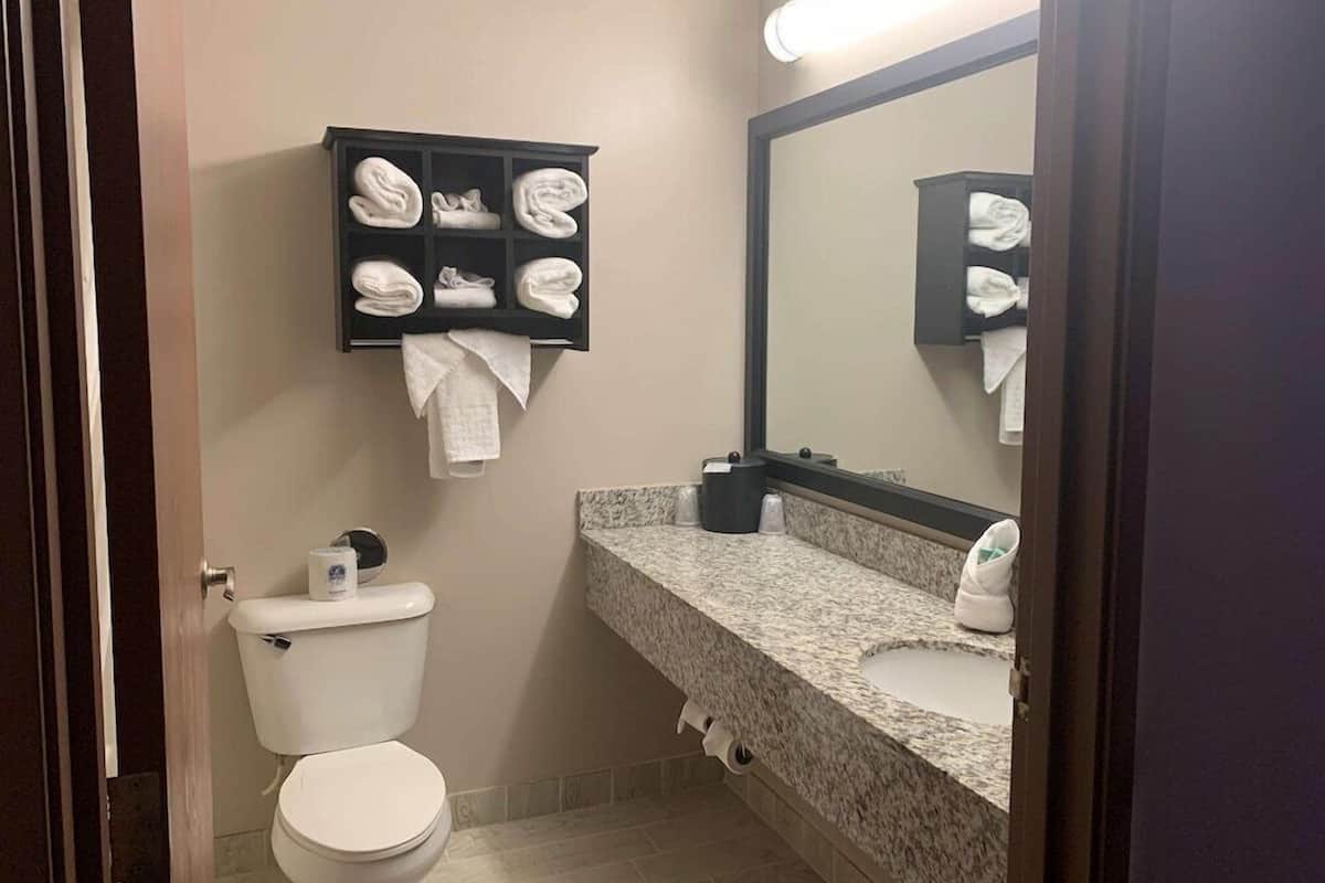 A bathroom with a toilet, a sink, a mirror, and a towel rack with folded towels.