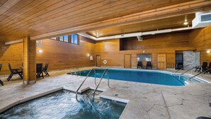 An indoor swimming pool with wooden walls and a stone floor, surrounded by chairs and a small hot tub.