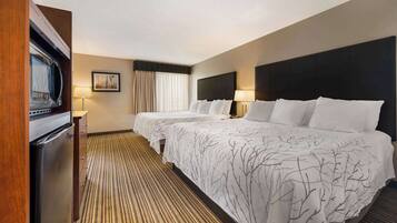 Een hotelkamer met twee bedden, een koelkast, een magnetron, een raam met gordijnen en een gestreept tapijt.