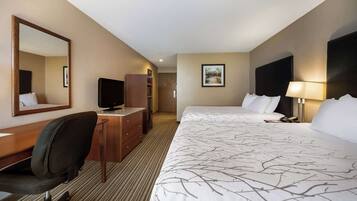 A hotel room with a large bed, a desk with a chair, a television, a dresser, and a lamp.