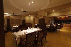 A dining area with multiple tables set for service, wooden chairs, and a high ceiling with recessed lighting. - Hotel Madhuban (Dehradun)