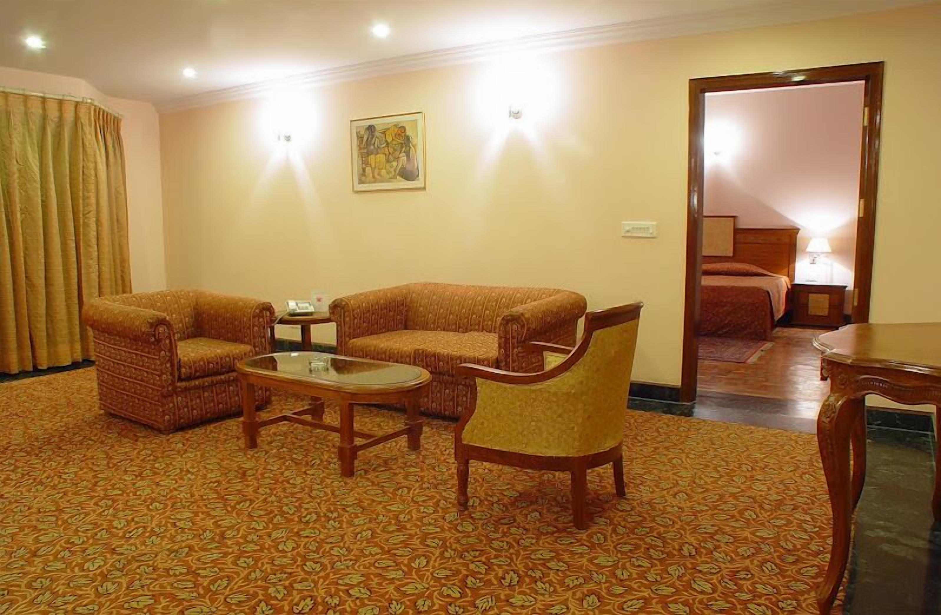 A hotel room with two sofas, a coffee table, and a chair. There is a painting on the wall and a door leading to another room.