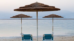 Een strand met twee blauwe stoelen onder een grote parasol en een kleinere parasol.