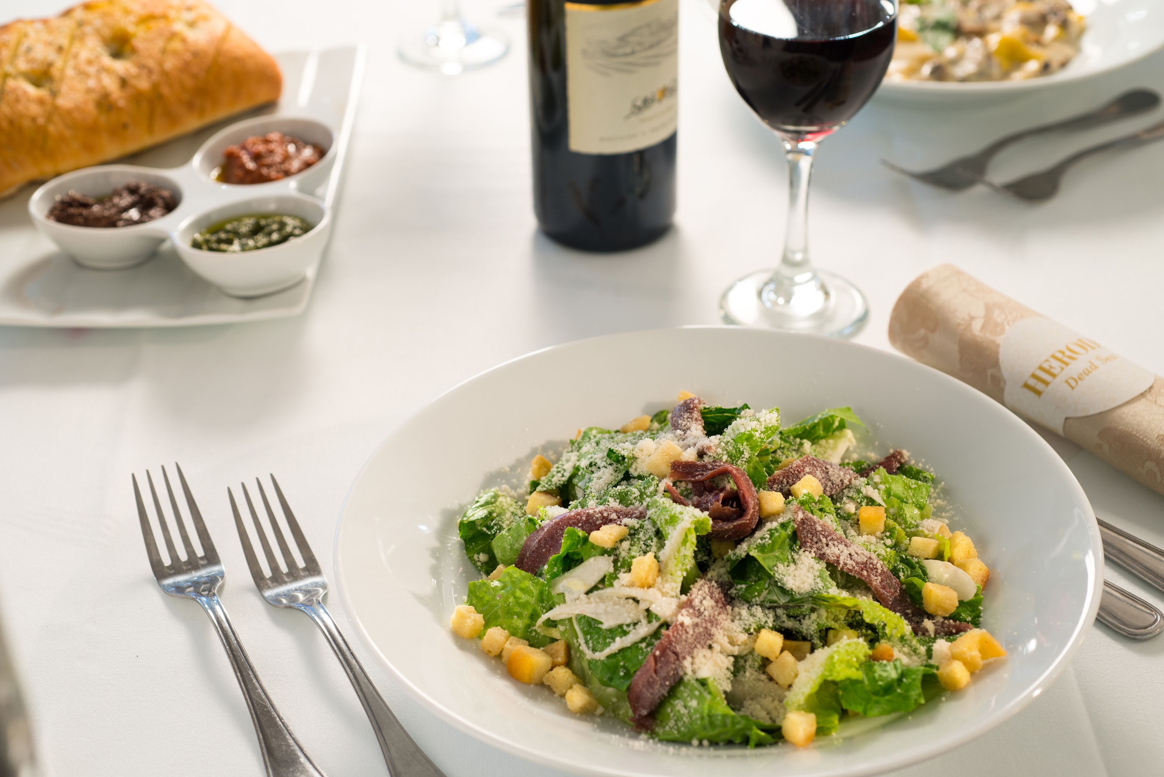 Una mesa con una ensalada en un bol, una botella de vino y una hogaza de pan.