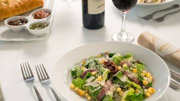 Una mesa con una ensalada en un bol, una botella de vino y una hogaza de pan.