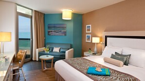Een hotelkamer met een bed, een bank, een kleine tafel, een stoel, een bureau, een lamp en uitzicht op zee.