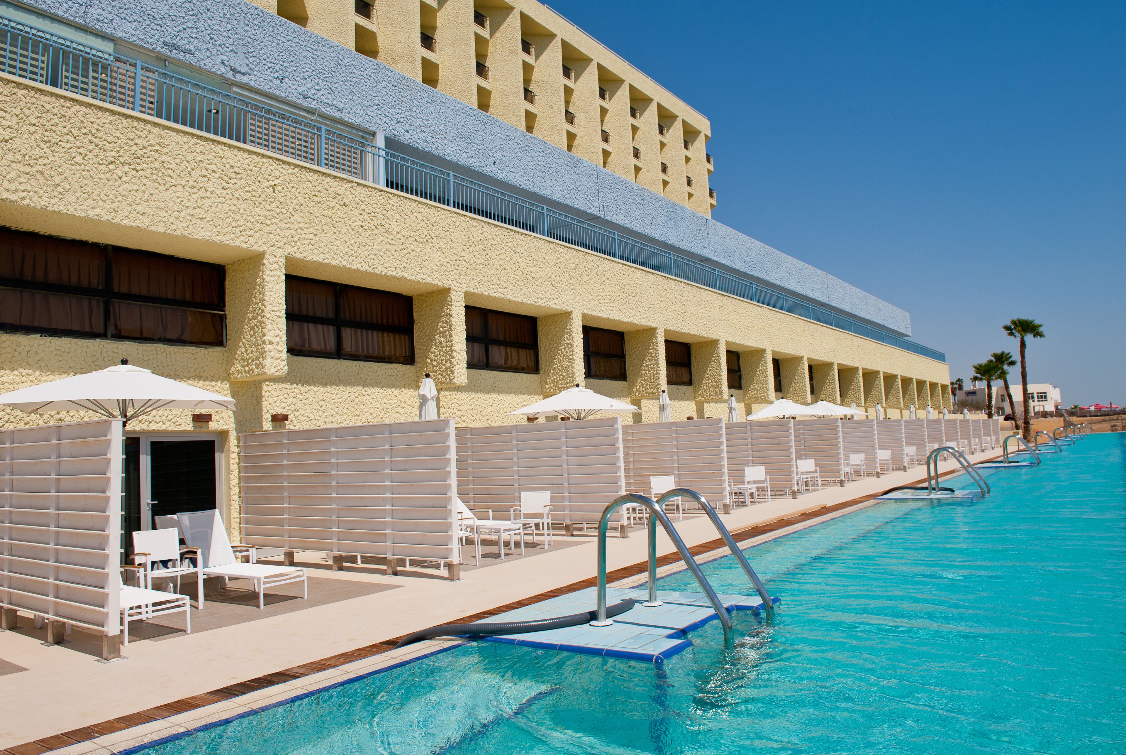 A hotel with a swimming pool, sun loungers, and umbrellas.