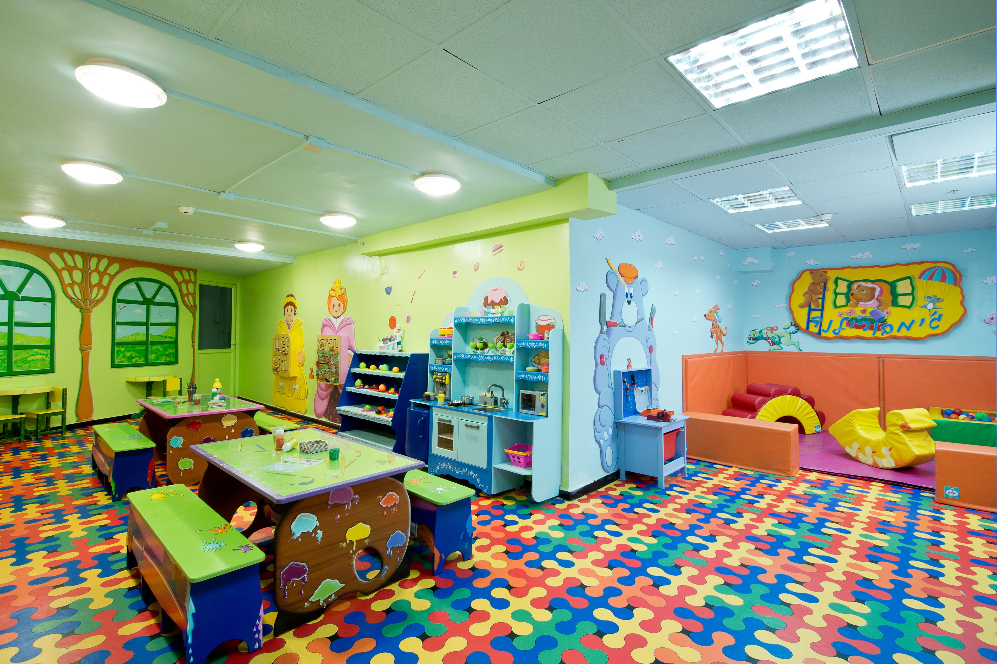 A brightly colored children's playroom with a multicolored floor, play tables, and various toys and bookshelves.