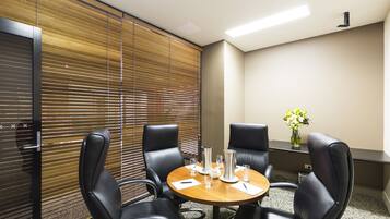 A conference room with a wooden table, four black leather chairs, a vase with flowers, and a window with blinds.