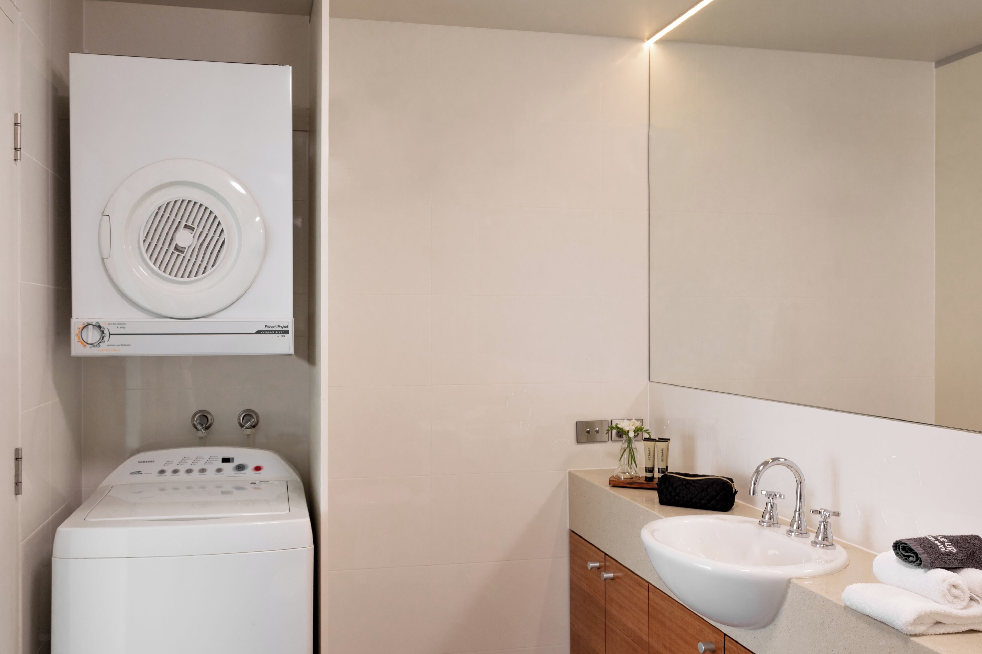 A modern bathroom with a built-in washer and dryer, a large sink, and a mirror above.