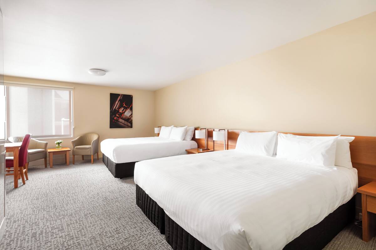 A hotel room with two beds, a desk, a chair, and a small table with a vase.