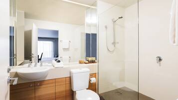Un baño moderno con ducha acristalada, lavamanos blanco y muebles de madera.