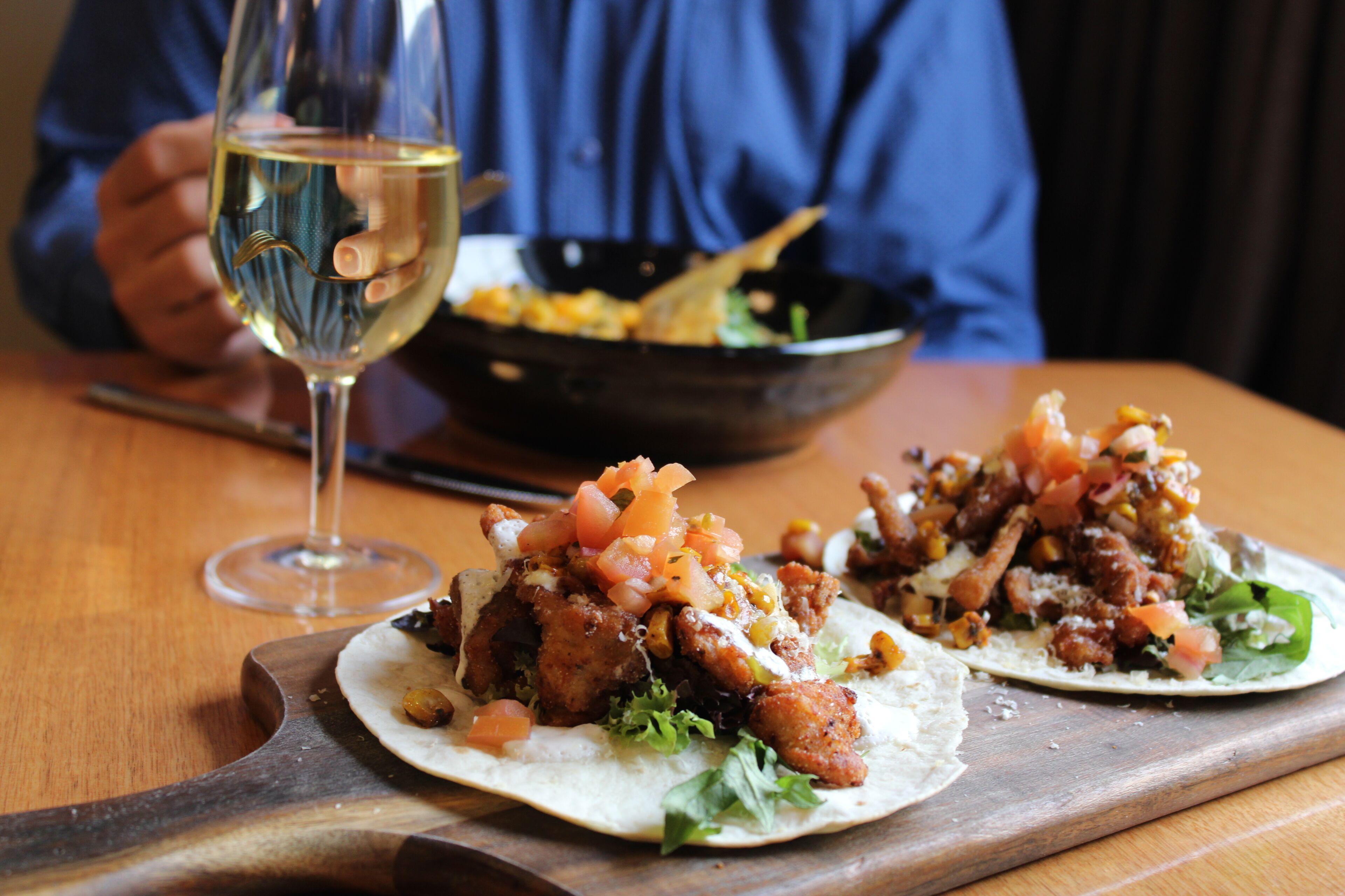 A wooden table with two tacos and a glass of white wine.