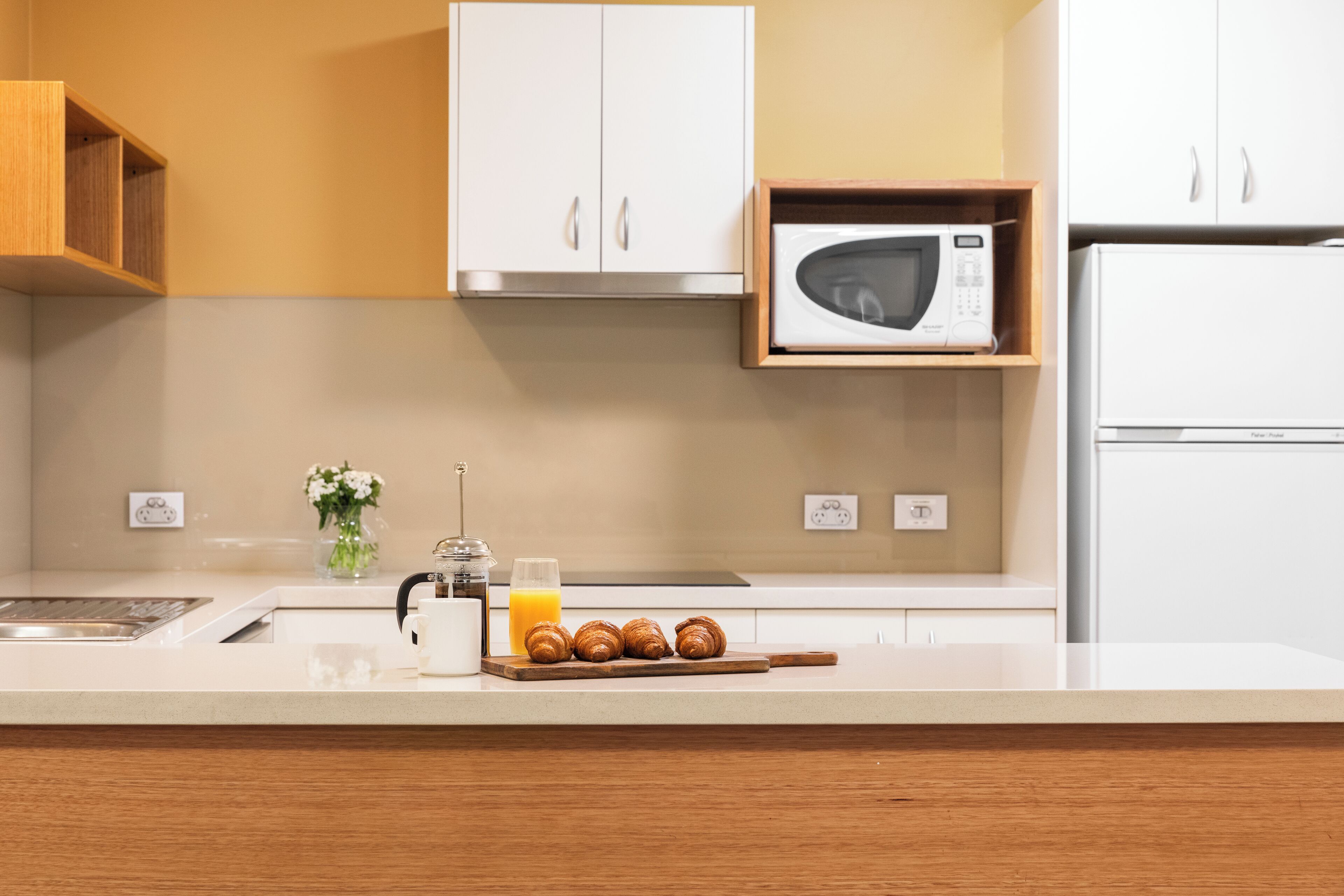 Une cuisine moderne avec des meubles blancs, un four à micro-ondes et un coin petit-déjeuner comprenant des croissants et du jus d’orange.