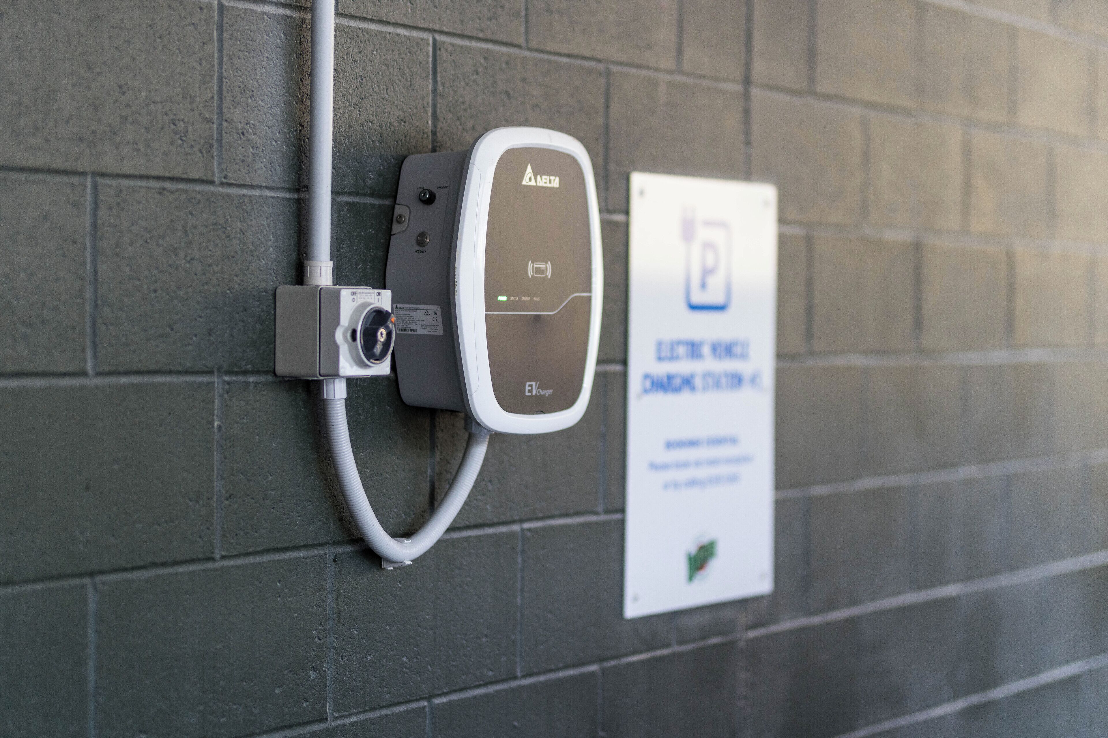 An electric vehicle charging station with a Delta EV charger and a sign indicating it is a public charging station.