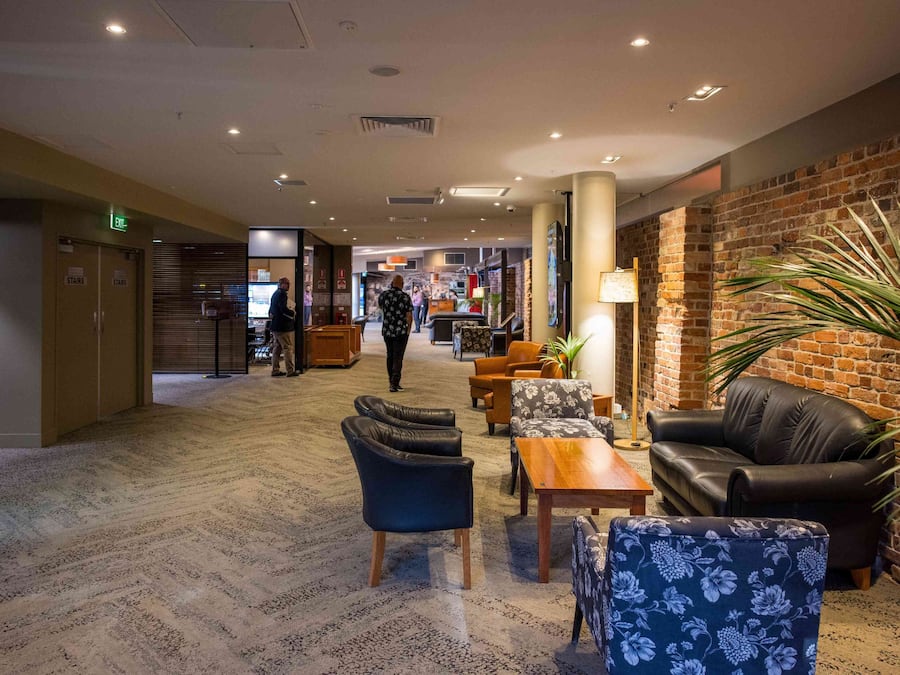 A hotel lobby with a carpeted floor, leather sofas, a wooden coffee table, and a brick wall.