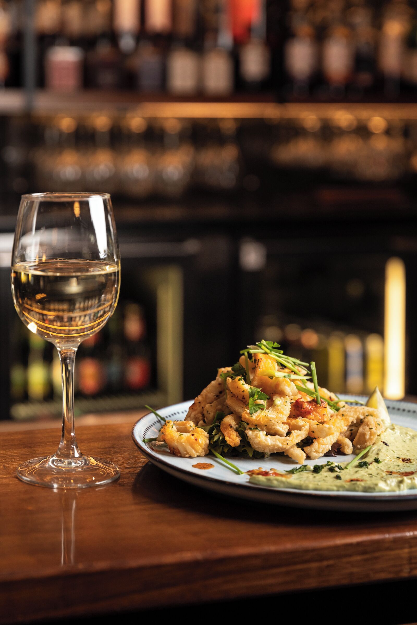 A glass of white wine and a plate of food on a wooden table.
