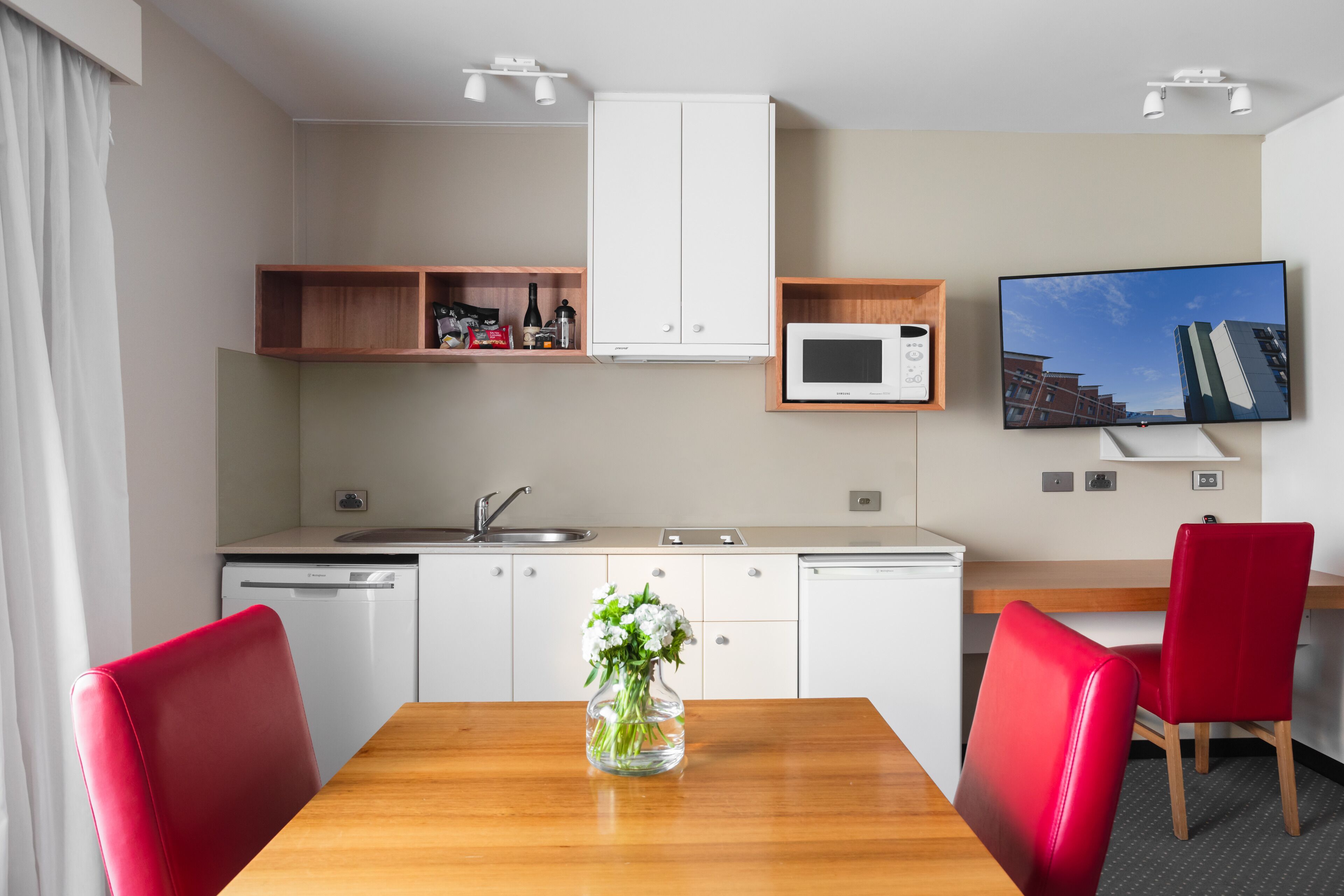 A modern kitchen with white cabinets, a microwave, and a dining area with a wooden table and red chairs.